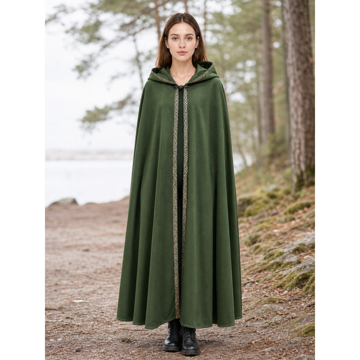 Green hooded cape with patterned front trim shown full-length on a model outdoors beside a wooded lakeshore