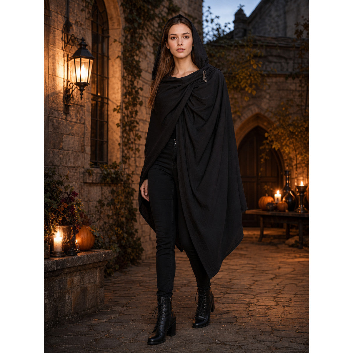 Black hooded cape with gathered front and pointed uneven hem, modeled outdoors by a woman in boots