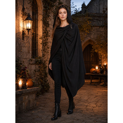 Black hooded cape with gathered front and pointed uneven hem, modeled outdoors by a woman in boots