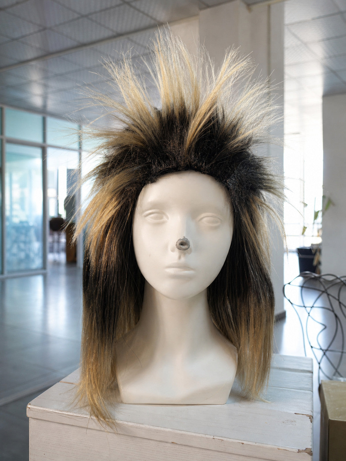 Costume wig with black and blonde spiky fibers and long straight side sections, displayed on a mannequin indoors