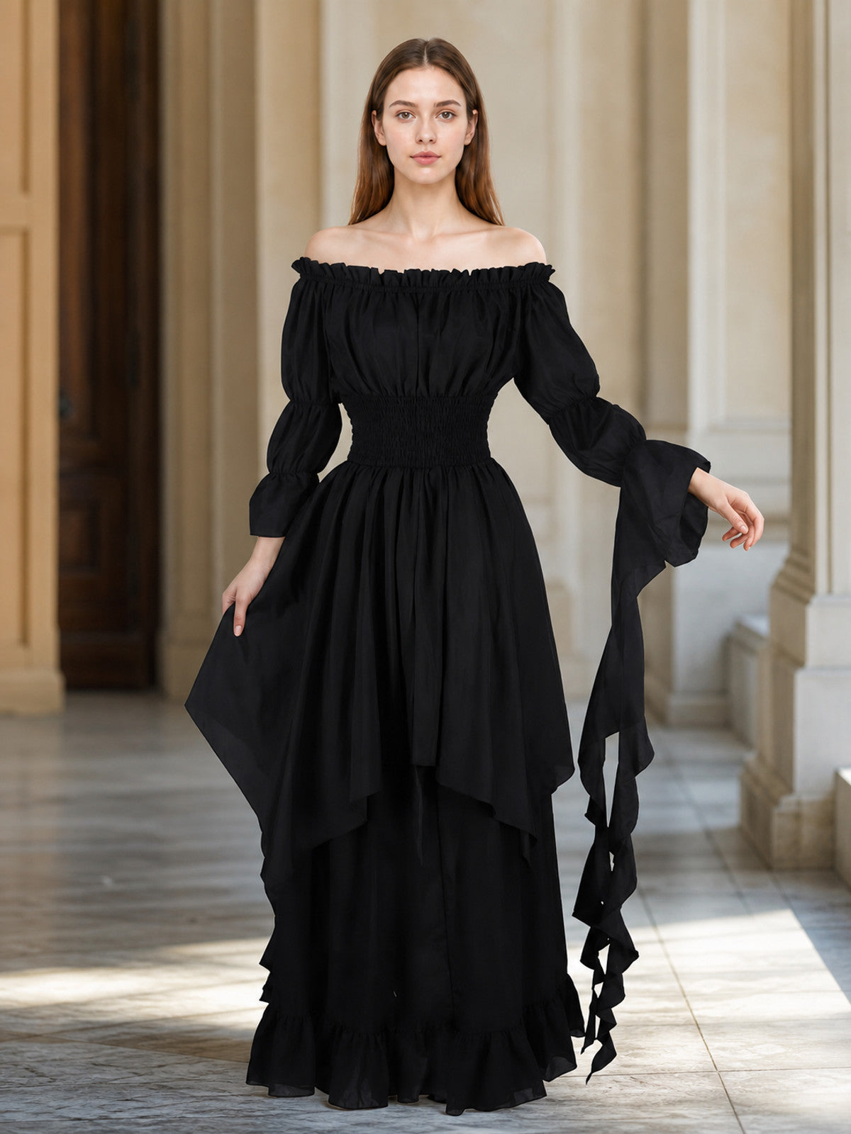 Full-body model wearing a black off-shoulder maxi dress in an interior setting, showing gathered sleeves, layered skirt, and trailing sleeve ties