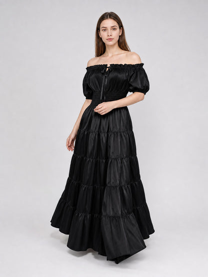 Black off-shoulder maxi dress shown on a model in a three-quarter pose, with puff sleeves, a fitted waist, and a tiered floor-length skirt