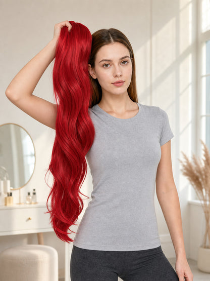 Red wavy ponytail hairpiece held beside a model in a bright indoor setting, showing its long length and flowing texture