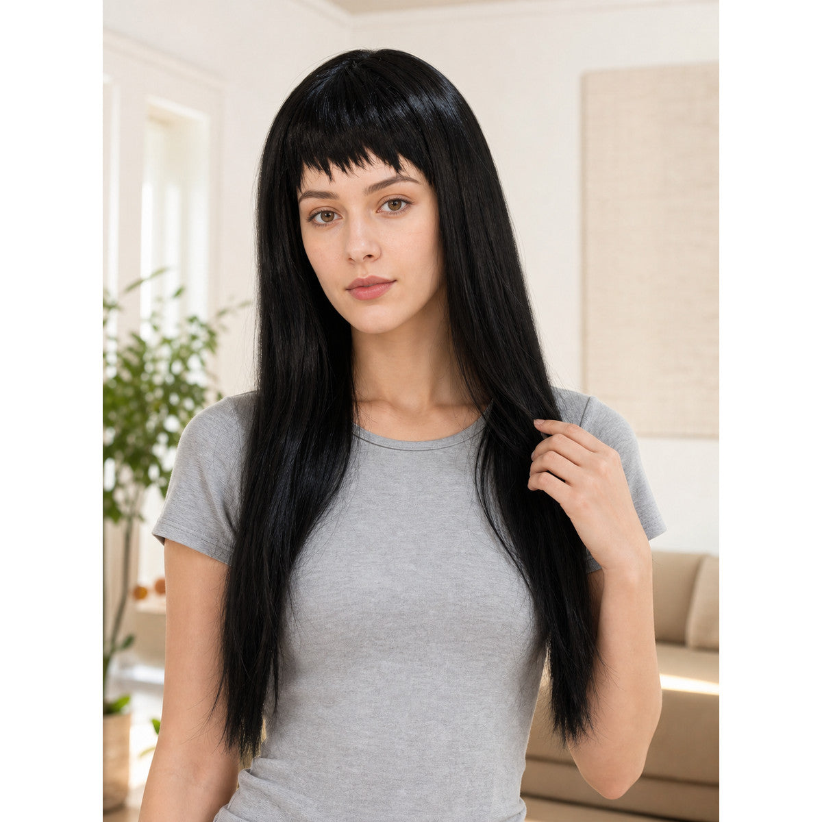 Black straight wig with blunt bangs shown on a model in a gray T-shirt in a furnished room