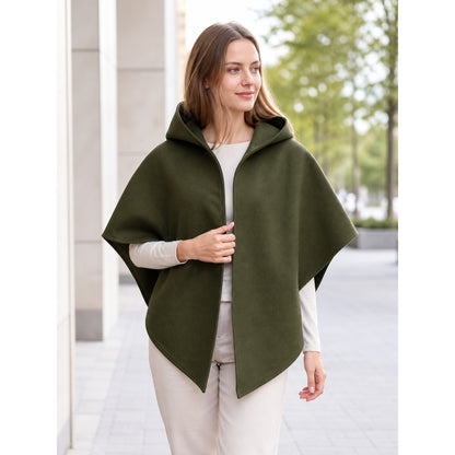 Model wearing an olive green hooded cape over white clothing in an outdoor setting, with the front opening held near the chest