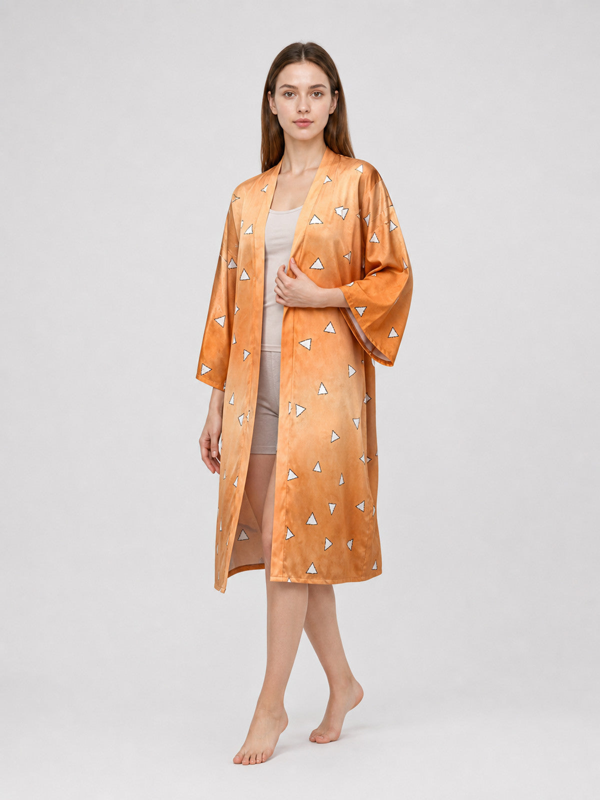 Three-quarter view of a model wearing an open orange patterned robe with wide sleeves over a white outfit