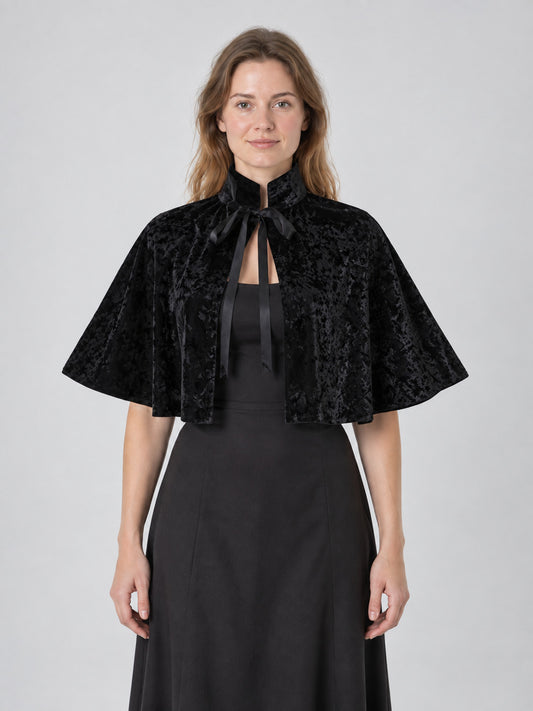 Model wearing a black velvet short cape with high stand collar and ribbon ties, front view