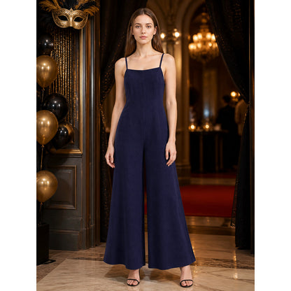 Dark blue wide-leg jumpsuit with thin shoulder straps, shown full-length on a model in an elegant decorated interior