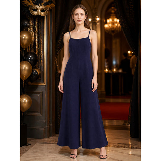 Dark blue wide-leg jumpsuit with thin shoulder straps, shown full-length on a model in an elegant decorated interior