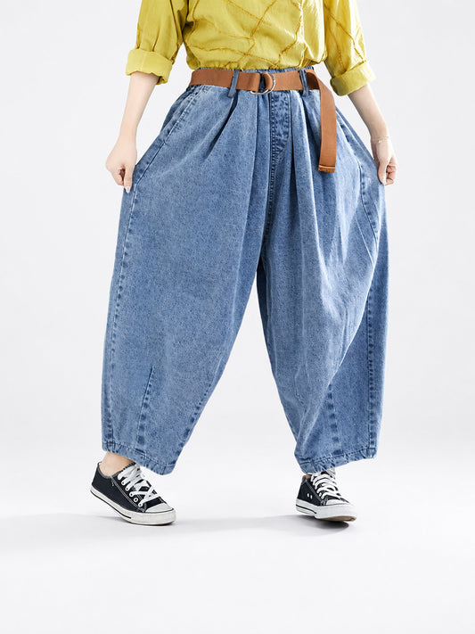 Blue denim pants shown from waist to shoes on a model, with pleated wide legs, side pockets, a brown belt, and black sneakers
