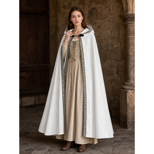 White hooded cape with colorful floral trim, shown full-length on a model over a beige dress in a stone interior