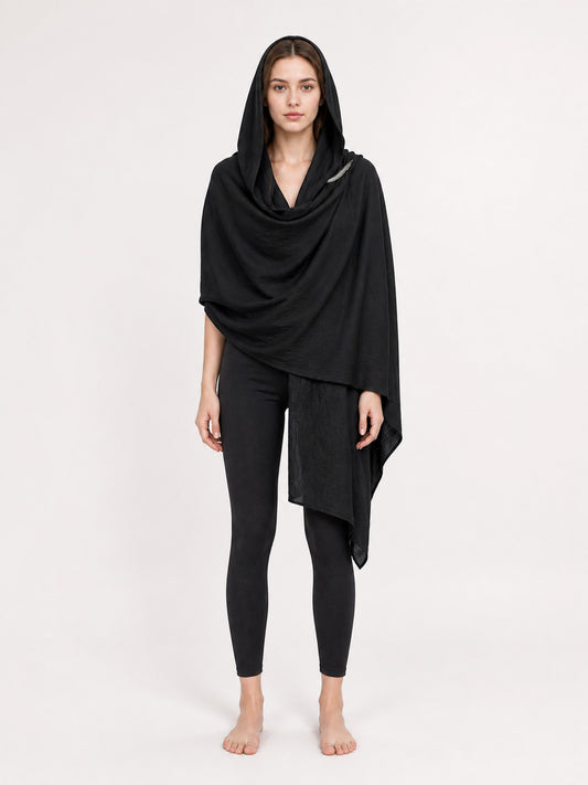 Black hooded cape with draped front and pointed asymmetrical hem, shown full-body on a model over black leggings