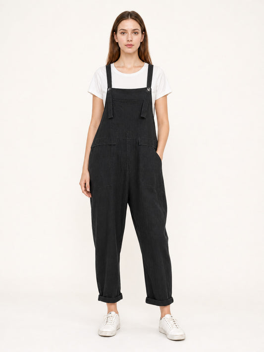 Black textured bib overalls shown full-body on a model with adjustable straps, chest pocket, side pockets and rolled cuffs