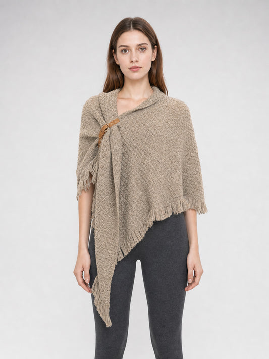 Beige woven cape on a full-body model, with a textured surface, side clasp, asymmetrical point, and fringe along the edges