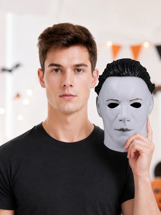 White face mask with molded features and black hair, held beside a man in a black shirt in a decorated indoor setting