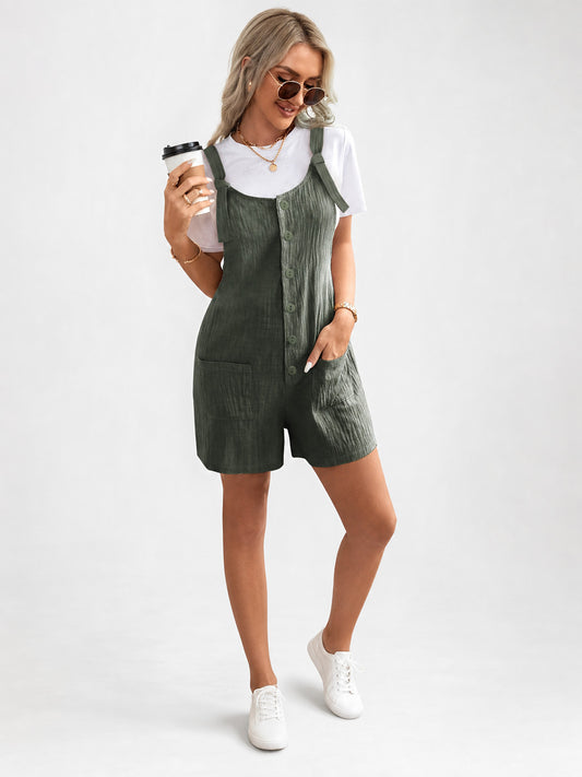 Olive green textured overall shorts worn over a white T-shirt in a full-body studio photo, with tied shoulder straps, front buttons and pockets
