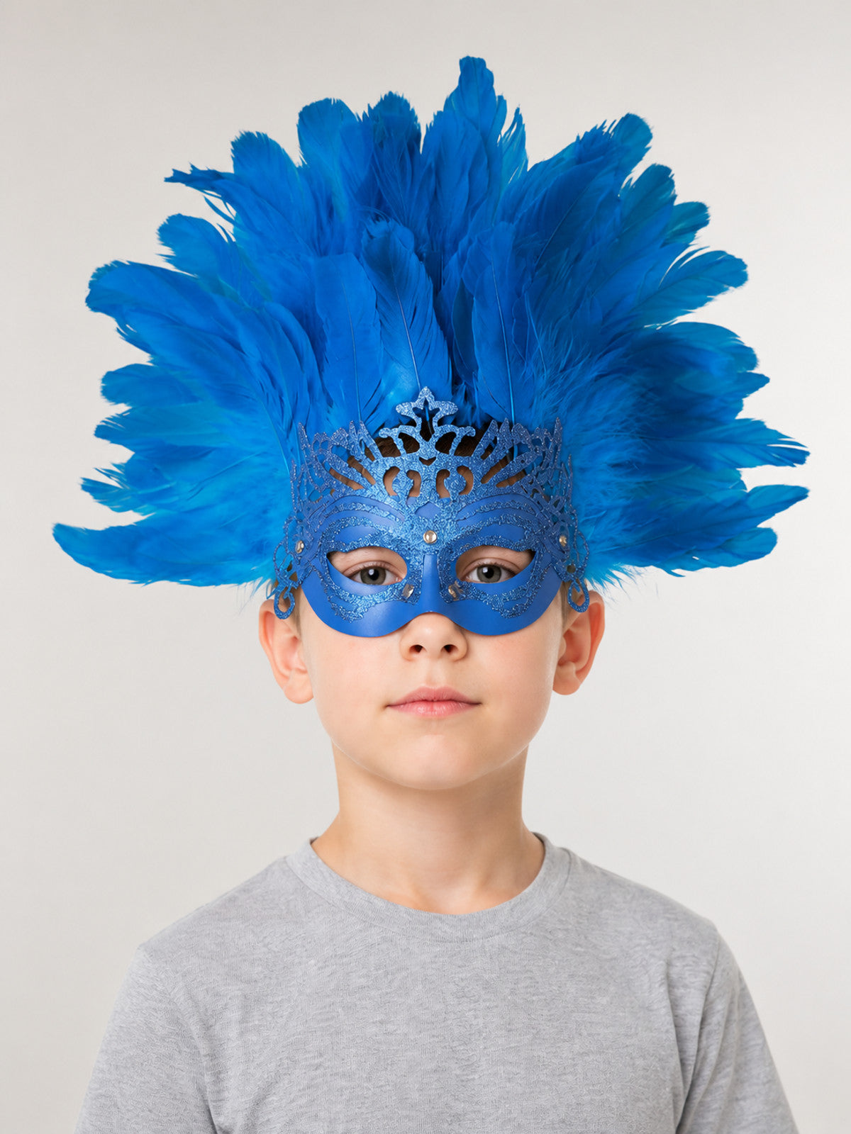 Blue feather masquerade mask with glittered eye covering and crown detail, shown worn by a child in a front-facing portrait