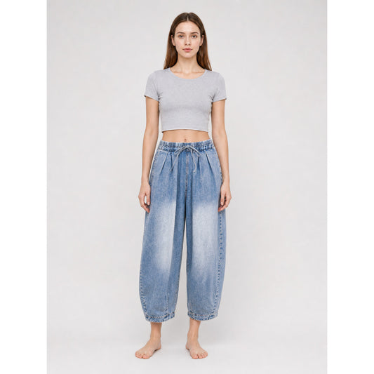 Light blue denim pants with an elastic drawstring waist and tapered ankles, shown full-length on a barefoot model against a plain background