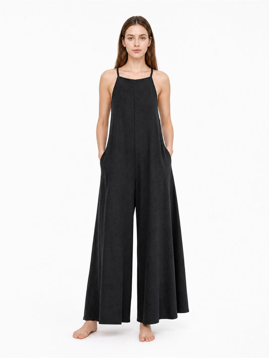 Black wide-leg jumpsuit with thin shoulder straps and side pockets, shown full-body on a model against a white studio background