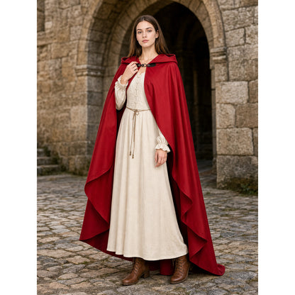 Red hooded cloak with layered edges, shown full-body on a model over a cream dress in front of a stone archway