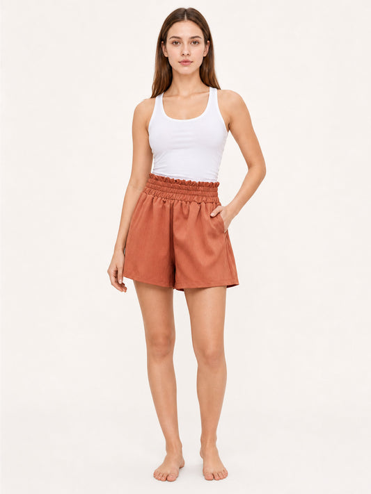 Terracotta shorts with a gathered high waistband and loose legs, shown full-body on a barefoot model against a plain background