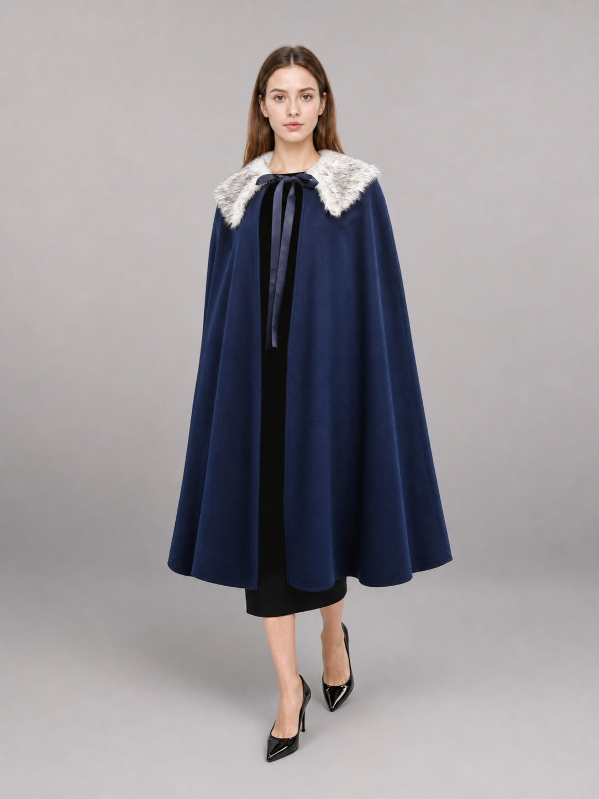 Navy blue cape with a white faux fur collar and ribbon tie, shown full-length on a model against a gray studio background