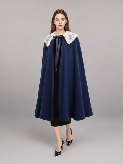 Navy blue cape with a white faux fur collar and ribbon tie, shown full-length on a model against a gray studio background