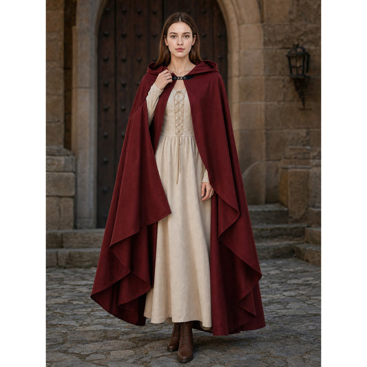 Burgundy hooded cloak with layered edges, shown full-length on a model over a cream dress in a stone courtyard