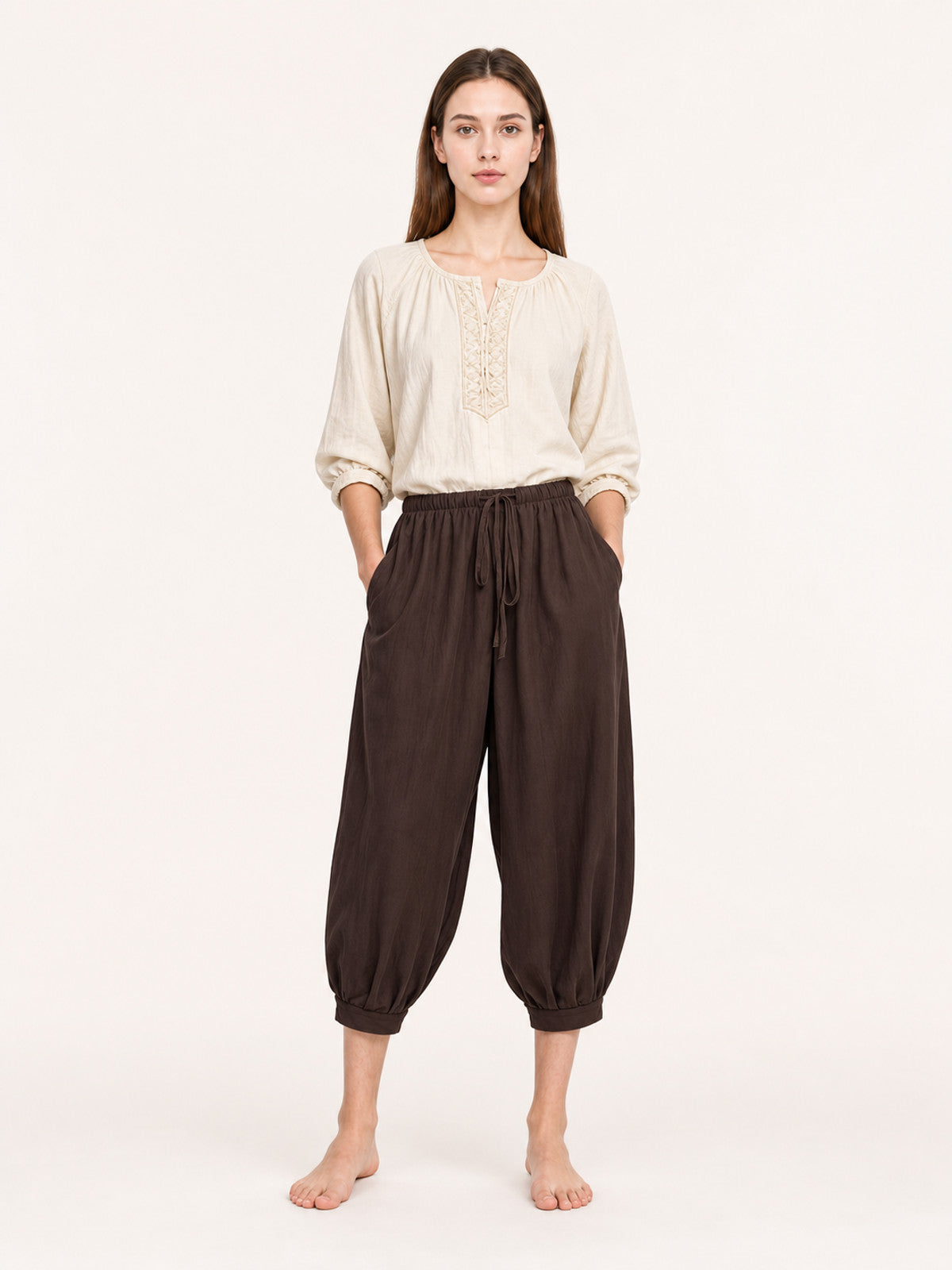 Brown cropped harem pants on a full-body model, with an elastic waist, front drawstring, side pockets and gathered ankle cuffs