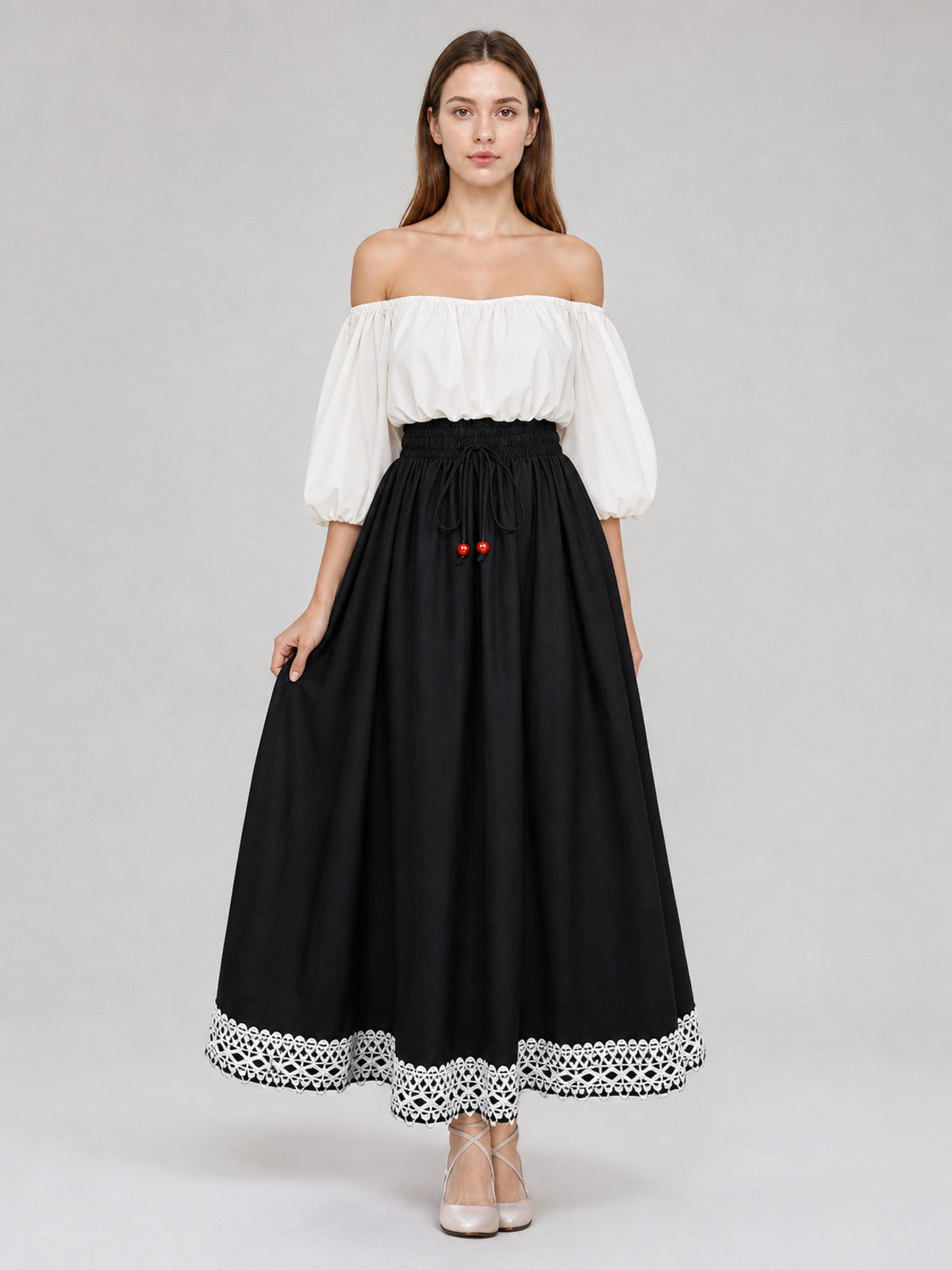 Full-body model wearing a black floor-length skirt with a gathered waist, red bead drawstrings, and white lace trim at the hem