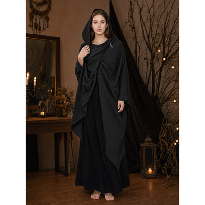 Black hooded cape with draped front panels, shown full-length on a barefoot woman in a candlelit room