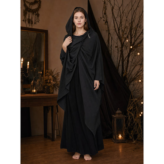 Black hooded cape with draped front panels, shown full-length on a barefoot woman in a candlelit room