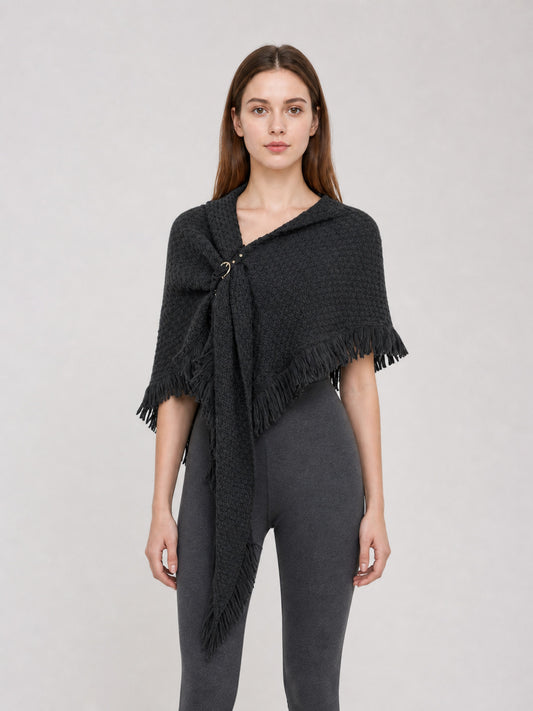 Black knitted poncho cape modeled full-body, with a triangular drape, long front point, side fringe, and ring fastening