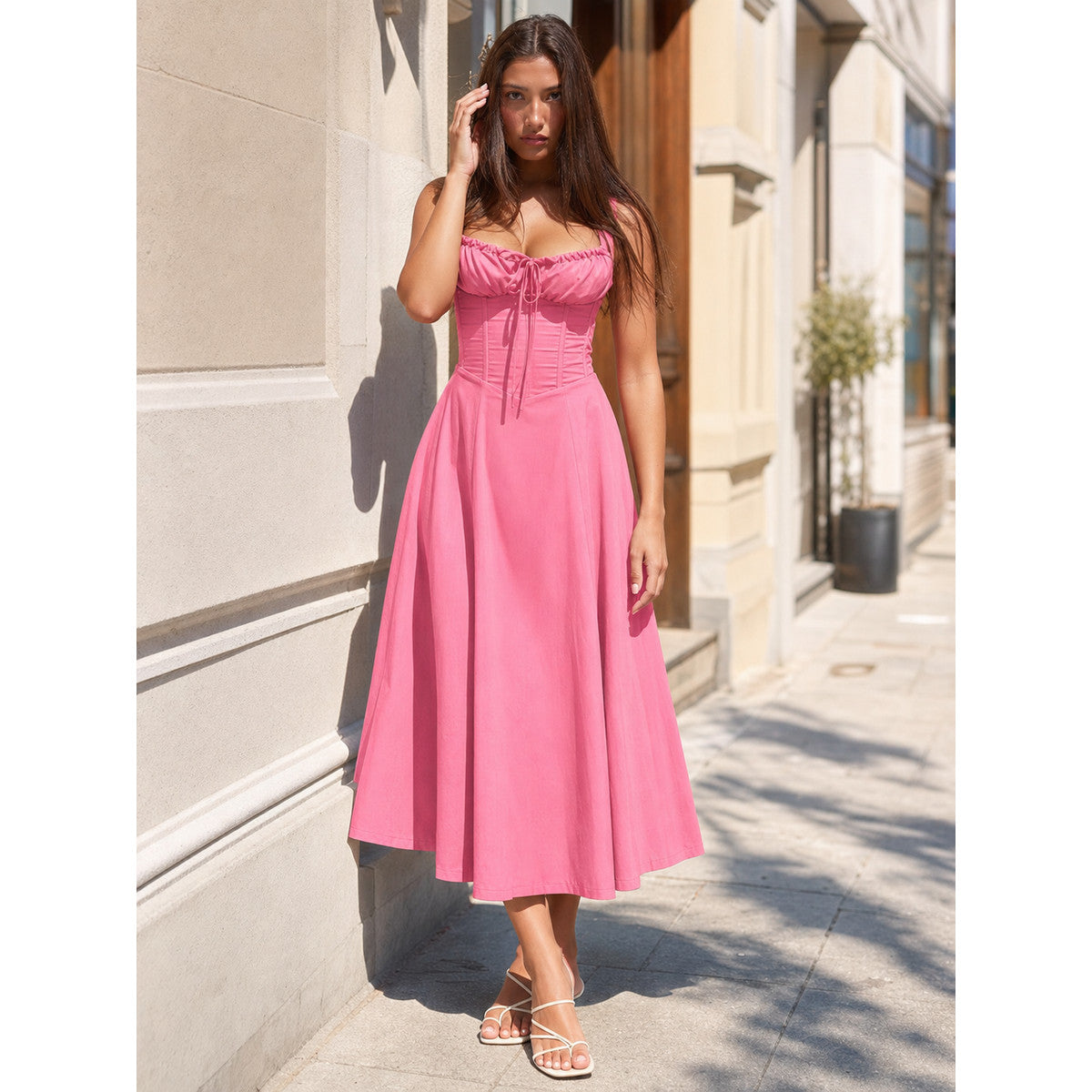 Women’s pink midi dress with a fitted bodice and a loosely flared skirt. The design features thin straps, vertical seam detailing, and decorative gathering at the bust. The tailored upper section flows smoothly into a voluminous flared hem,