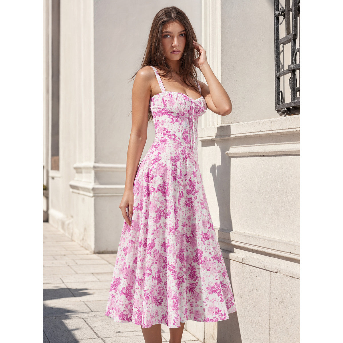Women’s midi dress with thin straps and a square neckline, featuring a front tie, visible pleats at the bodice, and a floral print on a white background with pink-red flowers. The waist-defined, flared-skirt silhouette creates a recognizabl