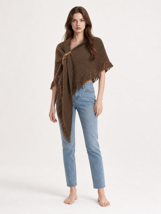 Brown textured triangular cape with long fringe and tan clasp, shown full-body on a model with blue jeans against a plain background