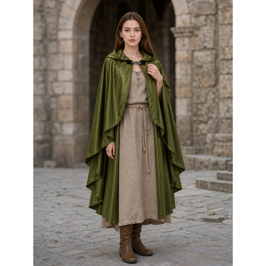 Green hooded cloak with layered pointed edges and front clasp, shown full-body on a model over a beige dress in a stone courtyard