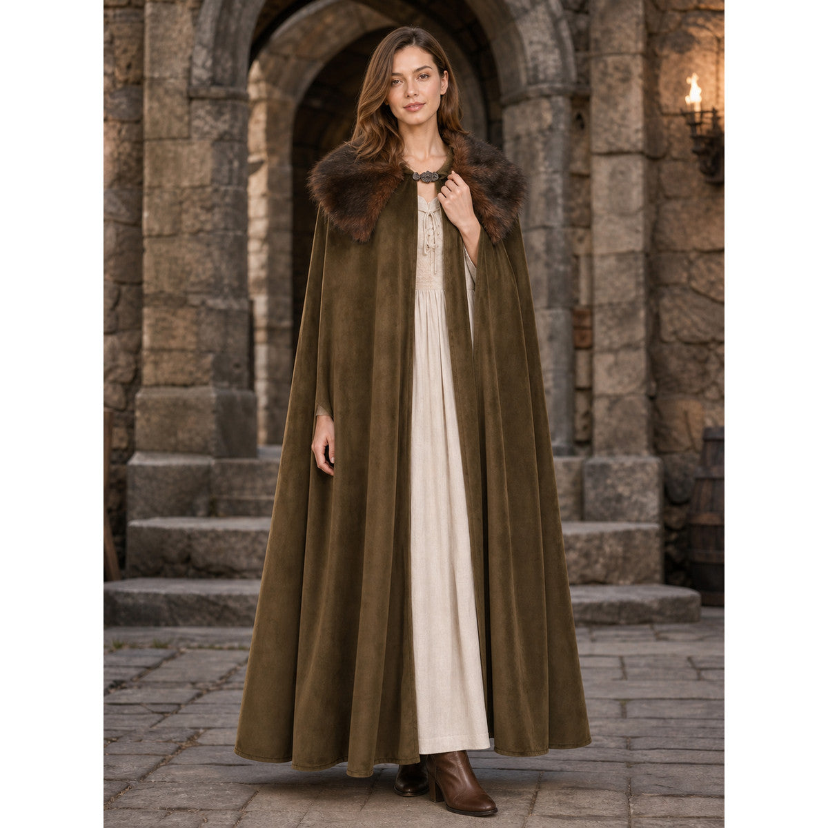 Brown suede-look open-front cape with a wide fur collar and front clasp, shown full-length on a model in a stone archway