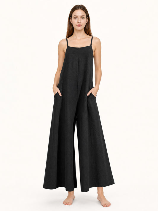 Black wide-leg jumpsuit with thin shoulder straps and side pockets, shown full-body on a barefoot model against a plain light background
