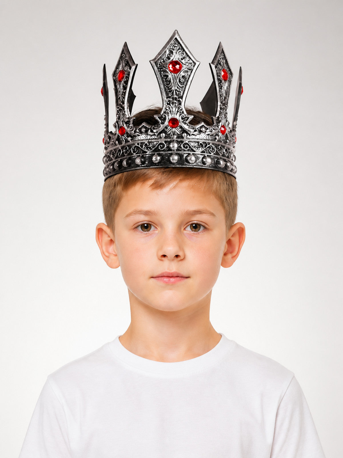 Silver-tone ornate crown with red stones and rounded studs shown on a child in a front-facing portrait