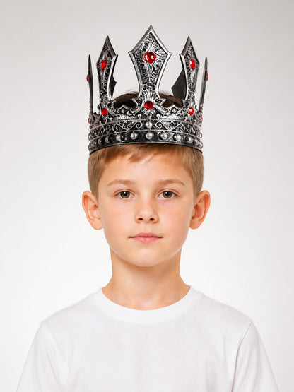 Silver-tone ornate crown with red stones and rounded studs shown on a child in a front-facing portrait