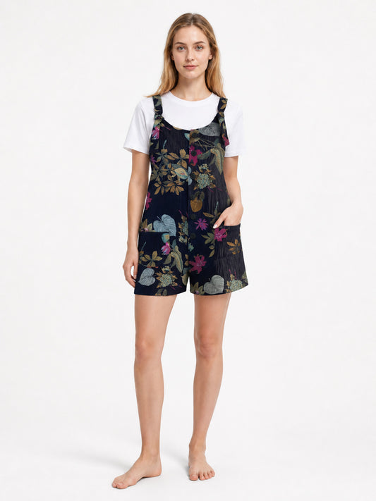 Dark navy floral overall shorts shown full-body on a model over a white T-shirt, with adjustable shoulder straps and front pockets