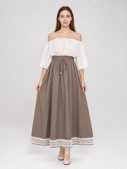Full-body model wearing a taupe maxi dress with a white off-shoulder gathered top, puff sleeves, drawstring waist, and white lace hem