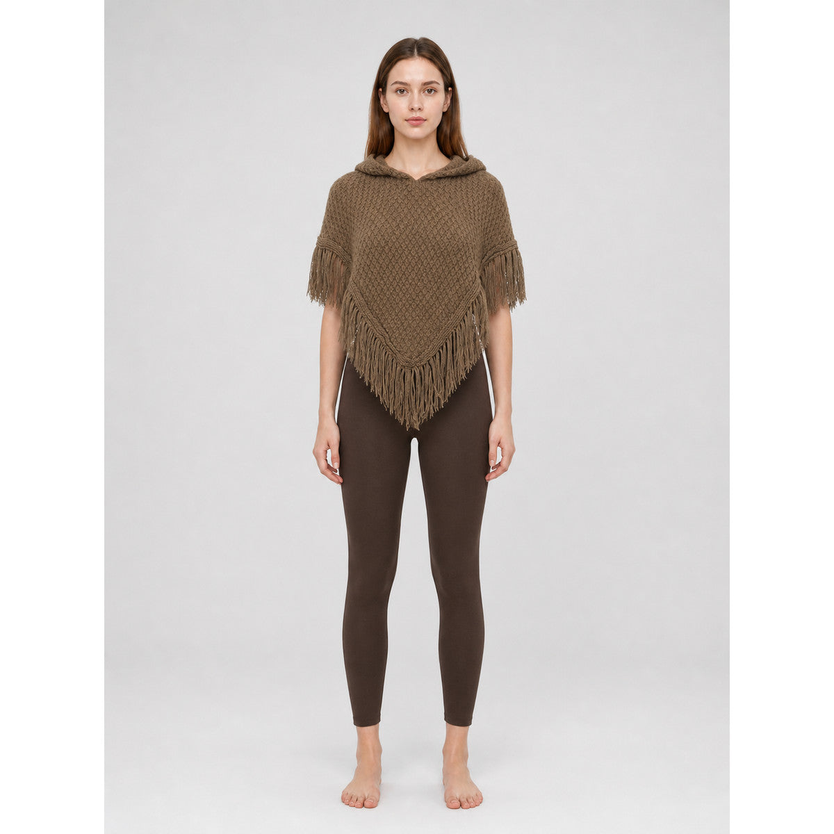 Brown knitted hooded cape with triangular front and fringe, shown full-body on a model against a light gray background