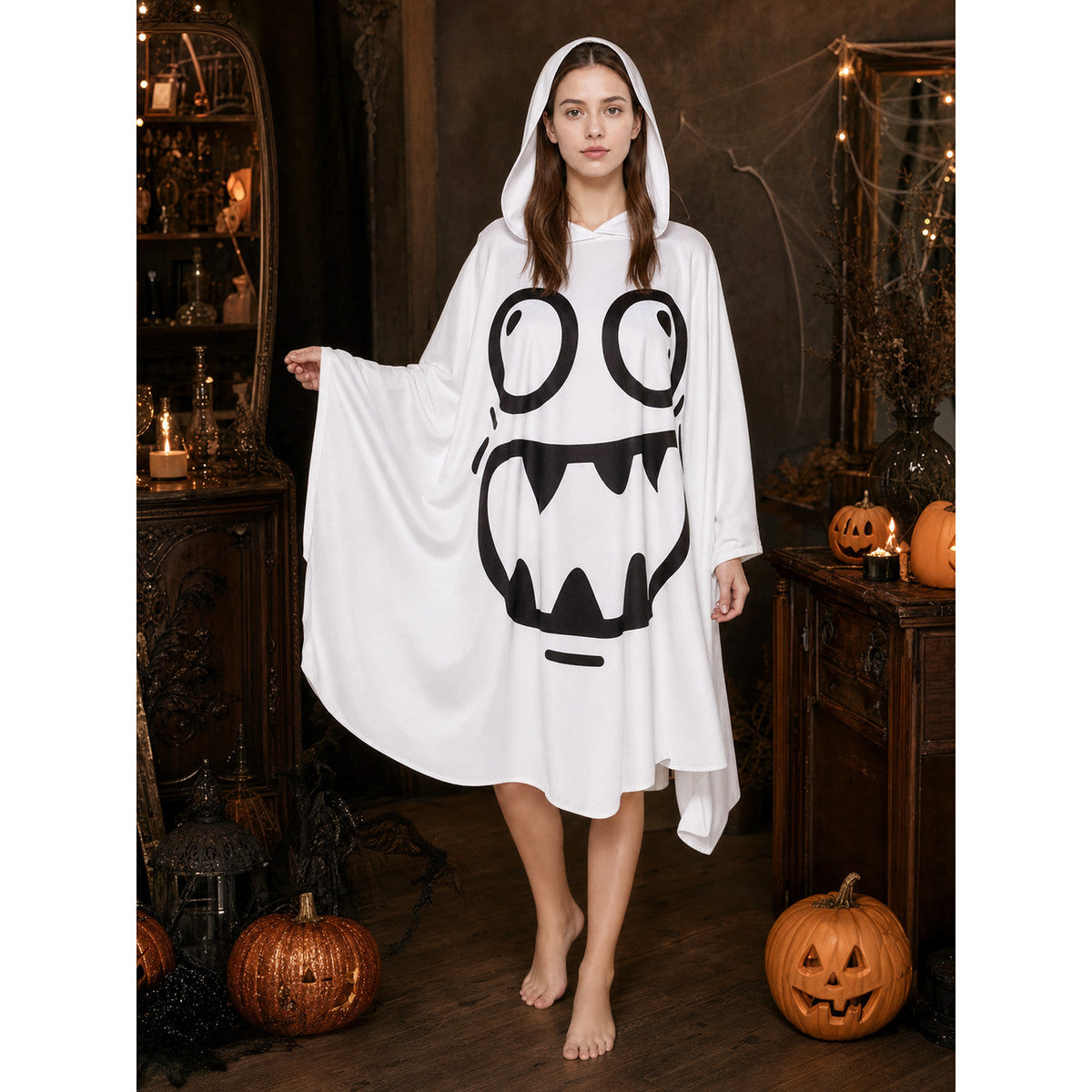 White hooded poncho costume with a black cartoon face and wide sleeves, modeled indoors among pumpkins and Halloween decorations