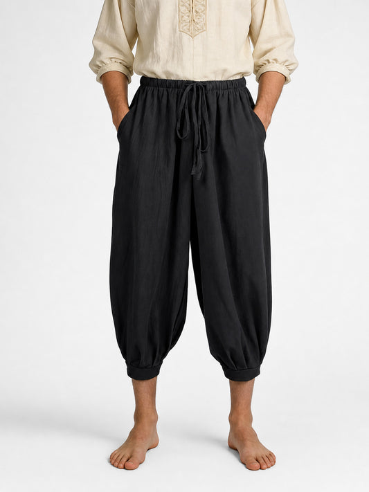 Black cropped harem pants shown from the waist down, with a drawstring waistband, side pockets, tapered legs, and gathered ankle cuffs
