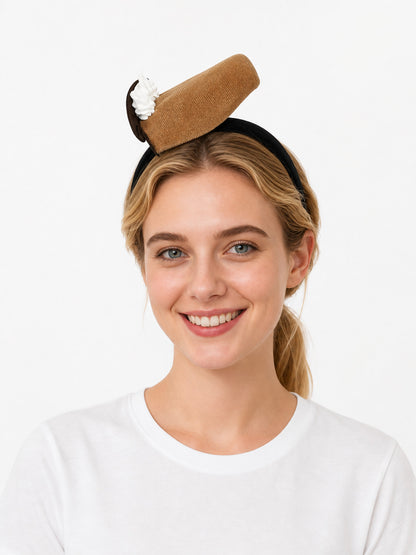Brown textured dessert-shaped headband with a white cream detail and dark brown end, shown on a smiling model