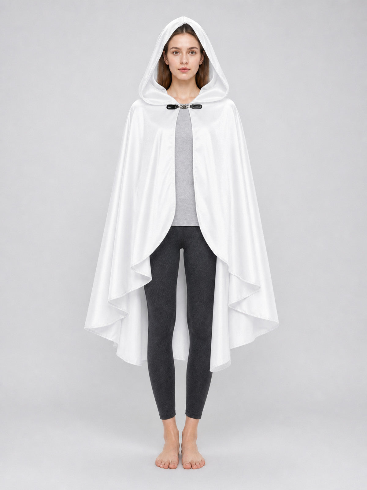 White hooded cape with layered pointed hem and black toggle closure, shown full-body on a barefoot model over a gray top and black leggings