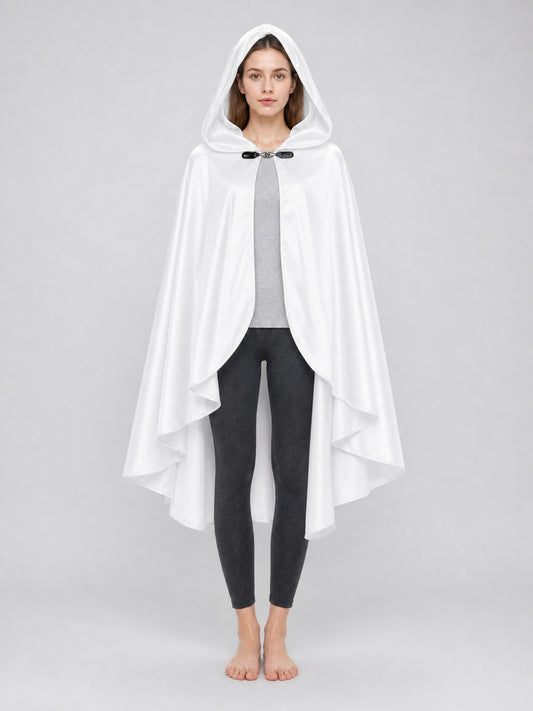 White hooded cape with layered pointed hem and black toggle closure, shown full-body on a barefoot model over a gray top and black leggings
