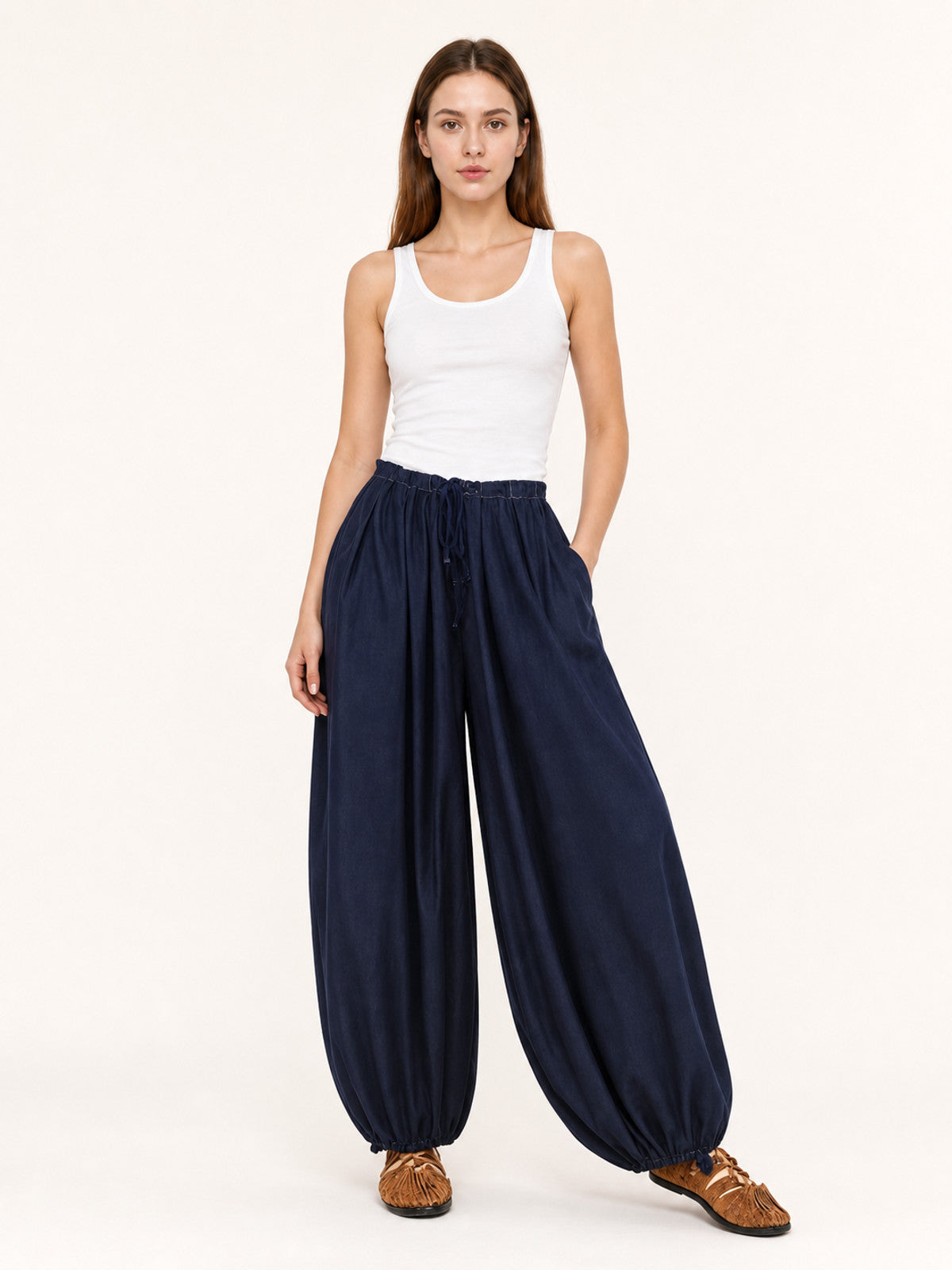 Dark blue pants shown full-body on a model, with an elastic drawstring waist, side pockets, wide legs, and gathered ankle hems